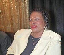 A smiling woman in a light-colored blazer and dark top.