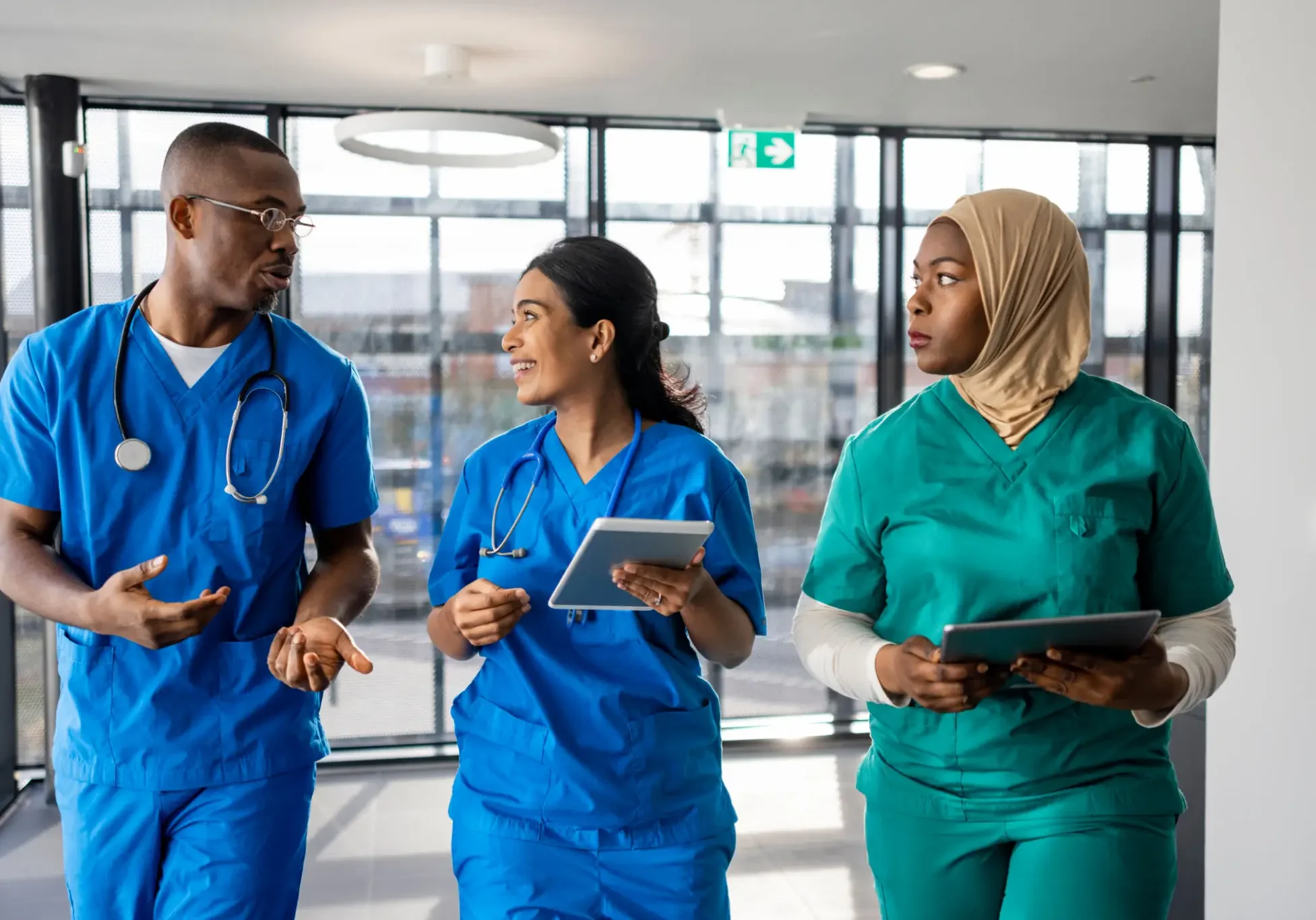Three healthcare professionals walking and discussing in a hospital corridor.