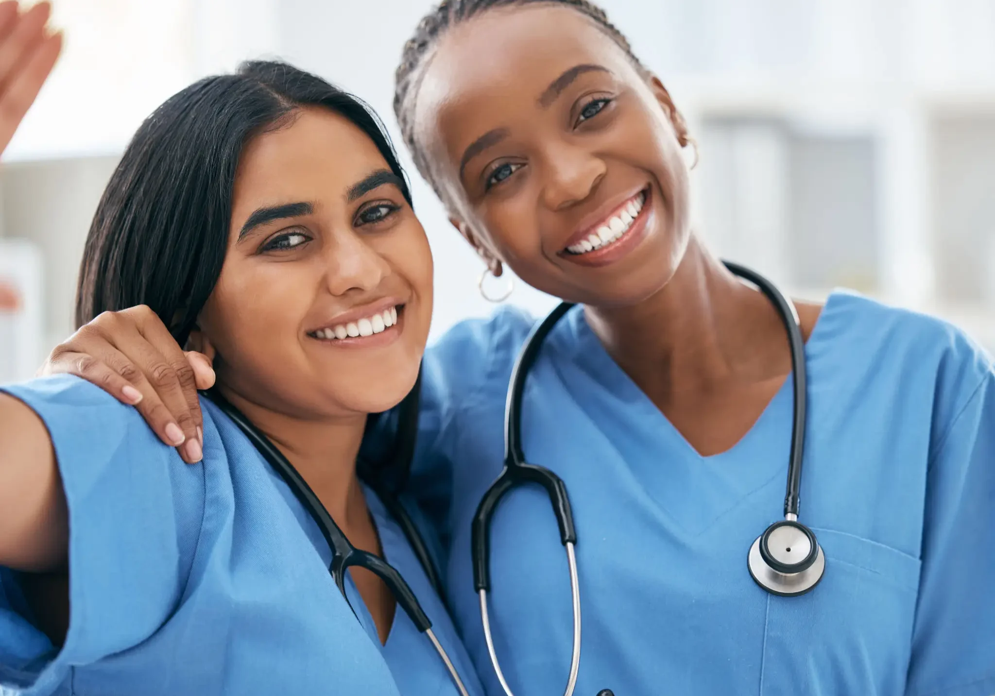 Two smiling female healthcare professionals in blue scrubs.